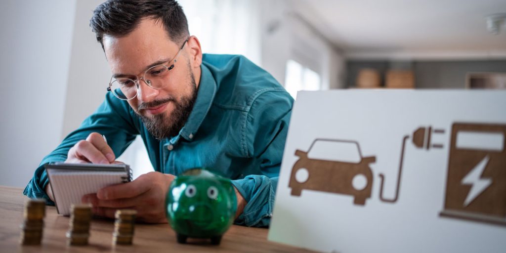 Man calculating electric vehicle running costs next to a piggy bank and EV icon.